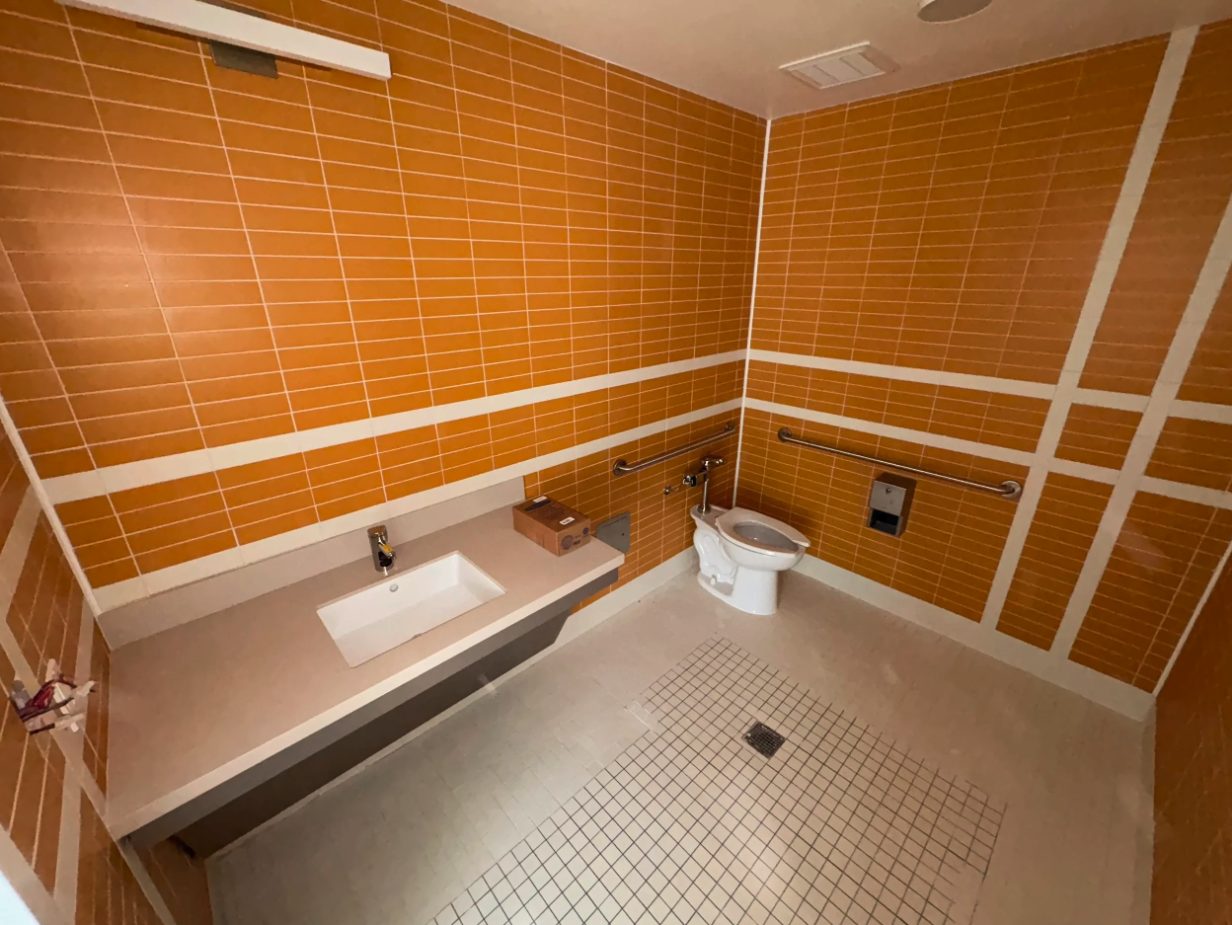 Finished ADA restroom in a healthcare clinic with flushometer toilet, lavatory counter, and floor drain