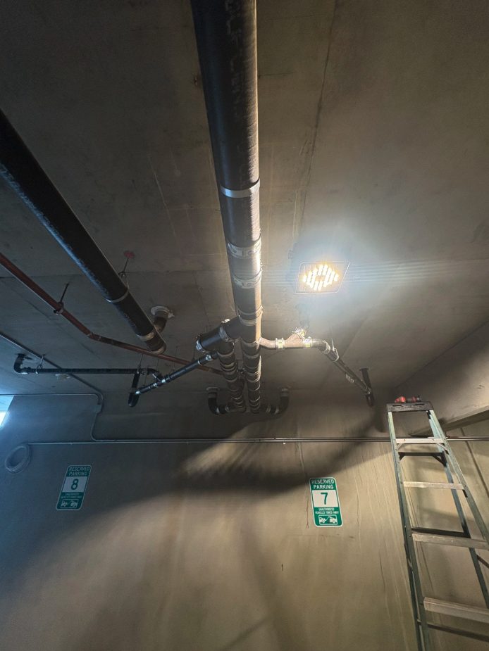 Cast iron drain piping hung from the ceiling of an office building's underground parking garage
