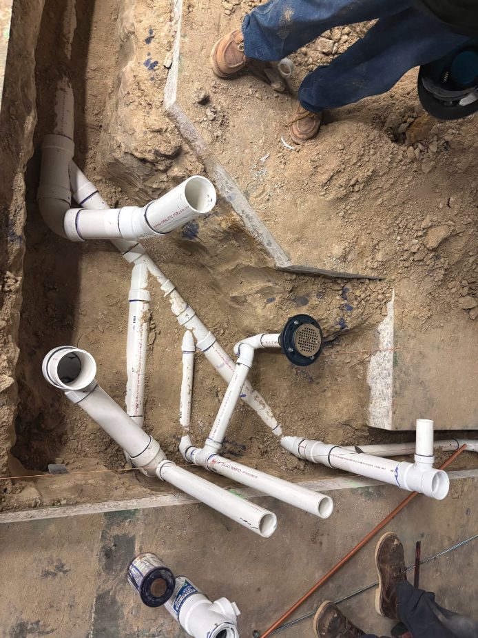 Underground waste piping and a floor drain for a clinic restroom, set in a trench cut through the slab